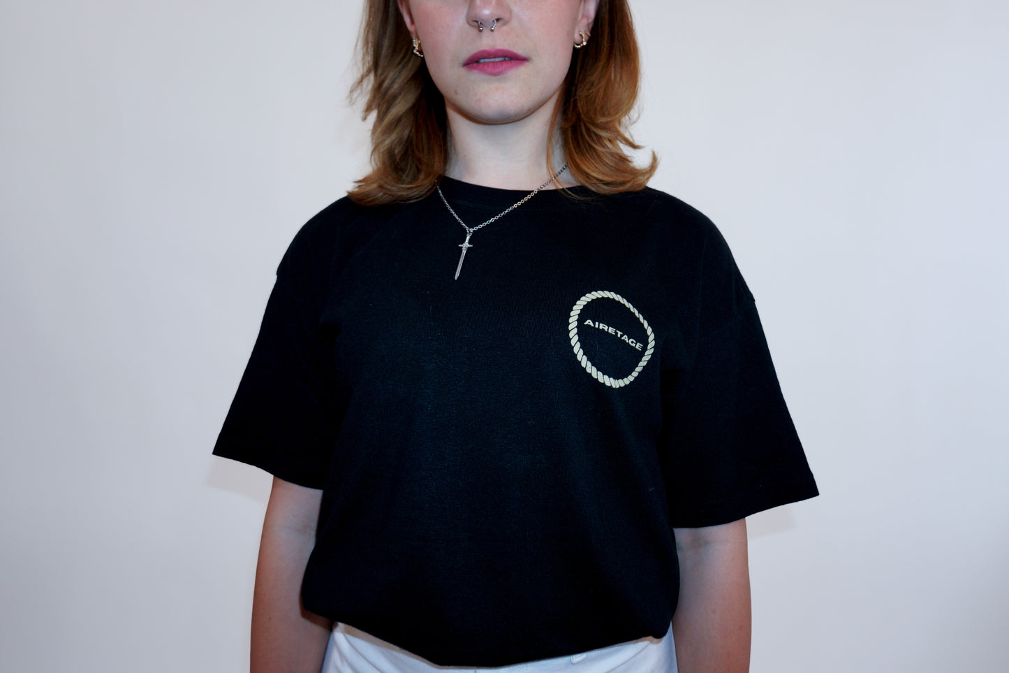 Person wearing a black t-shirt with a logo on a plain background