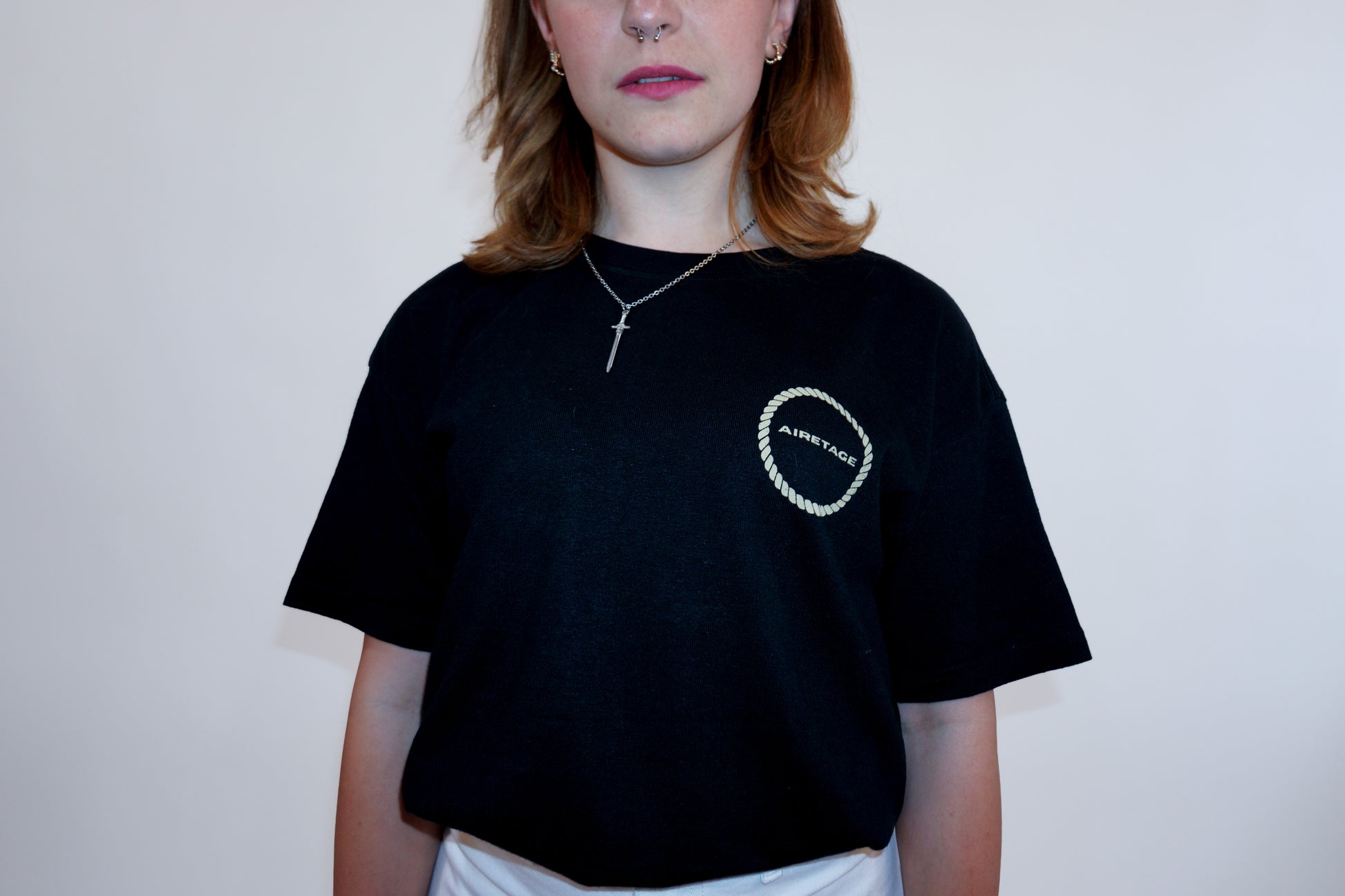 Person wearing a black t-shirt with a logo on a plain background